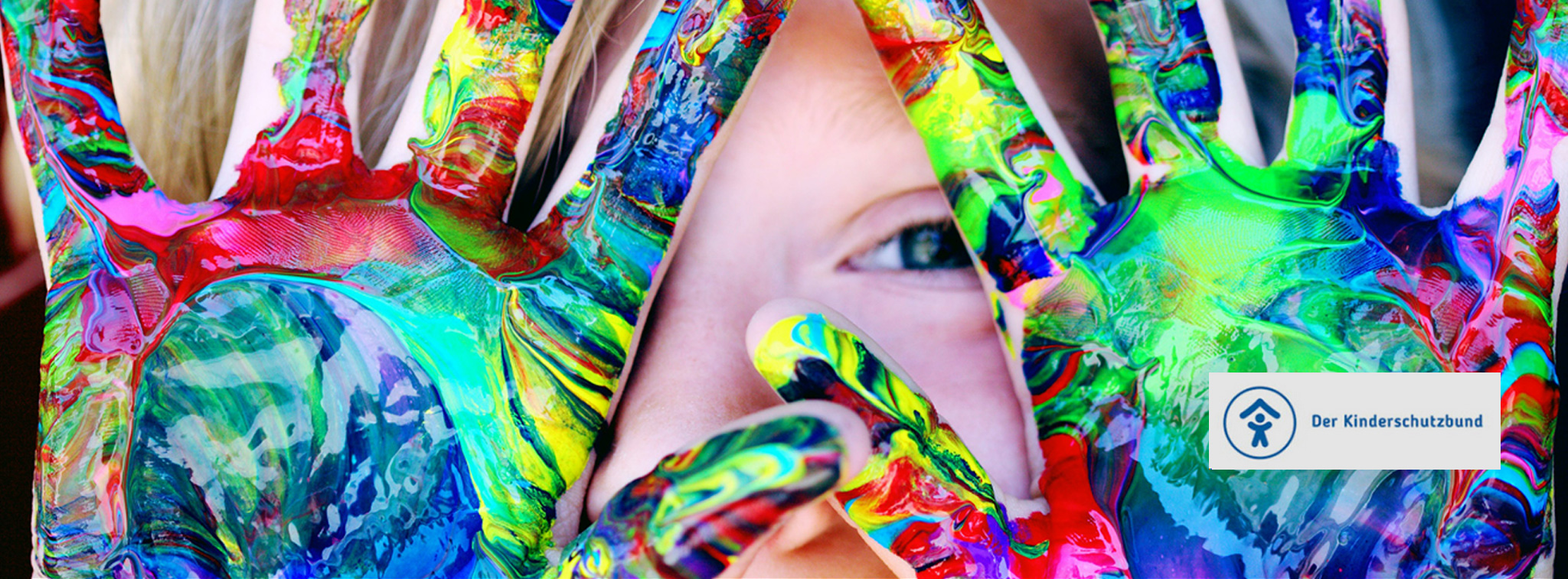 Kind zeigt bunt bemalte Hände vor dem Gesicht