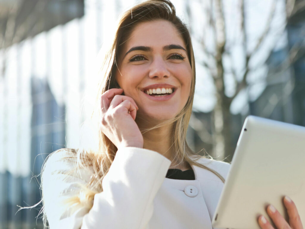 Frau in weißem Mantel telefoniert lächelnd im Freien