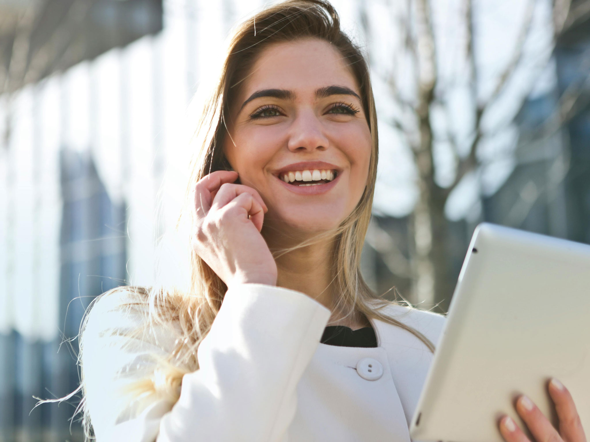 Frau in weißem Mantel telefoniert lächelnd im Freien