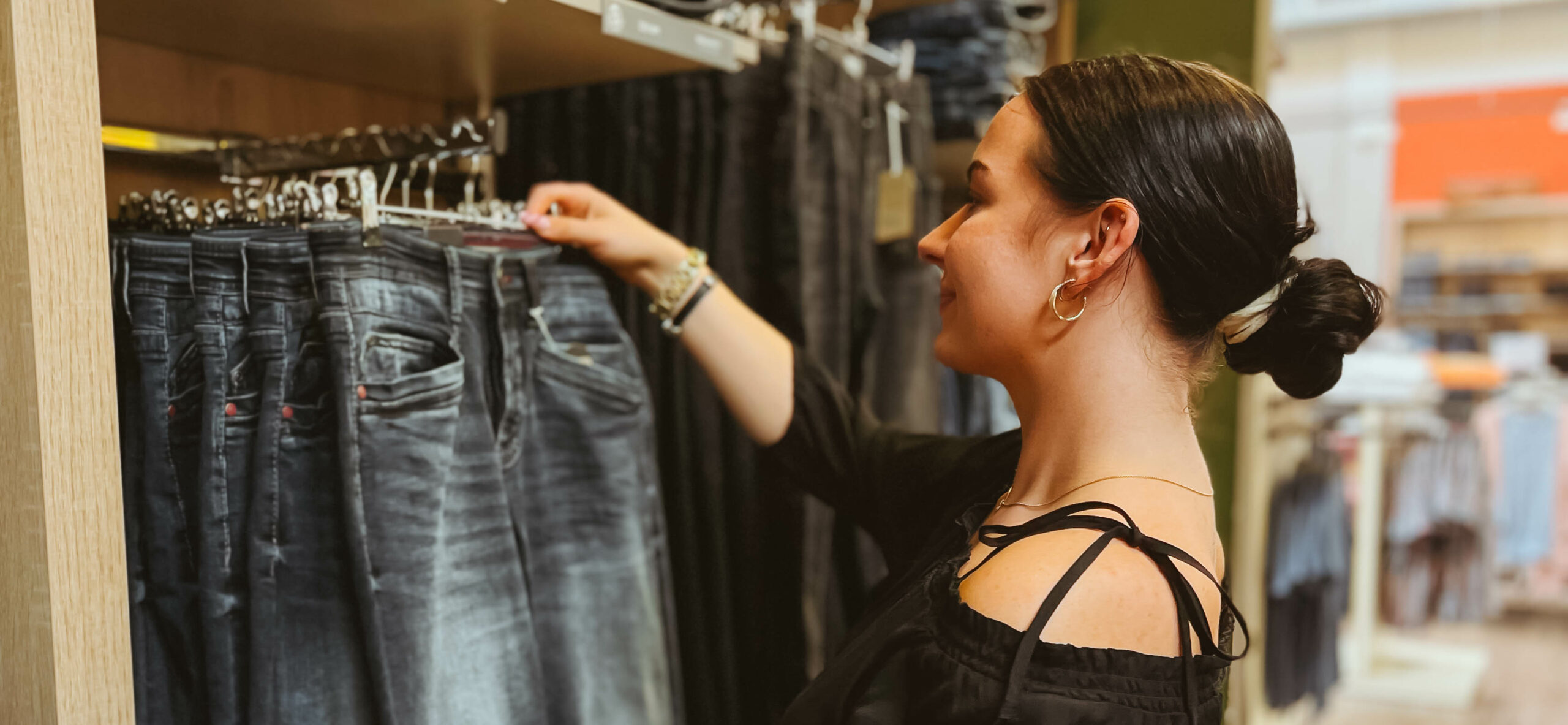 lächelnde junge Verkäuferin schaut sich Jeanshose an