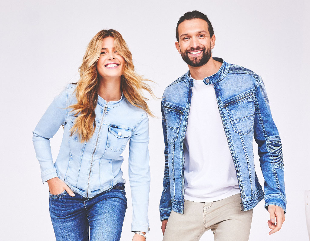 Mann und Frau lächeln in blauen Jeansjacken vor weißem Hintergrund